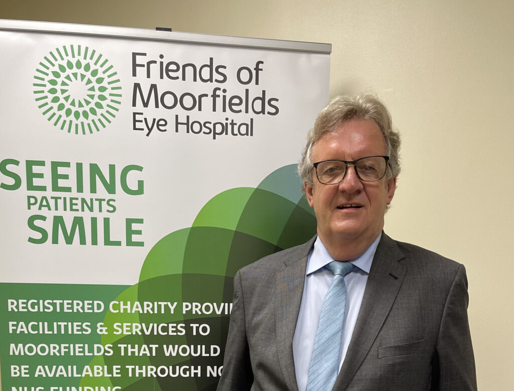 A photograph of Tim Hutchings standing next to a green Friends of Moorfields banner.