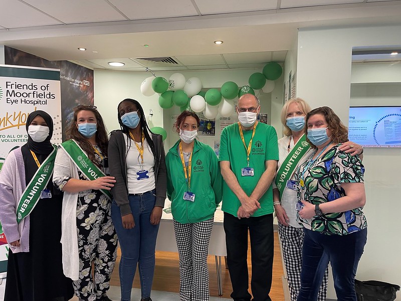 A photograph of several people in green volunteer uniforms posing together, with green balloons behind them.