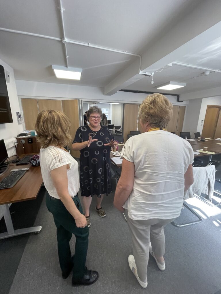 A photograph of a woman smiling and gesturing as she explains something to two listeners.