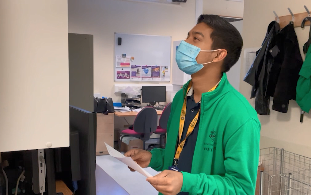 A photo of a volunteer carrying a piece of paper and looking for something on a shelf.