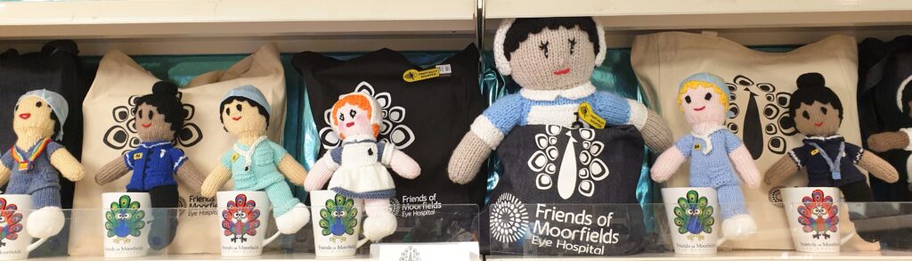 A row of several knitted dolls on a shelf in the shop. Some of them wear modern scrubs and others wear old-fashioned nurses' uniforms.