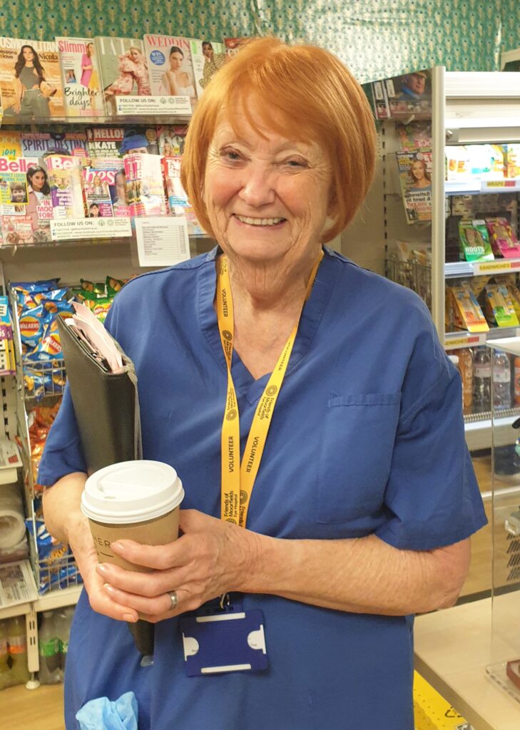 Brenda smiling in scrubs in the Friends of Moorfields shop.