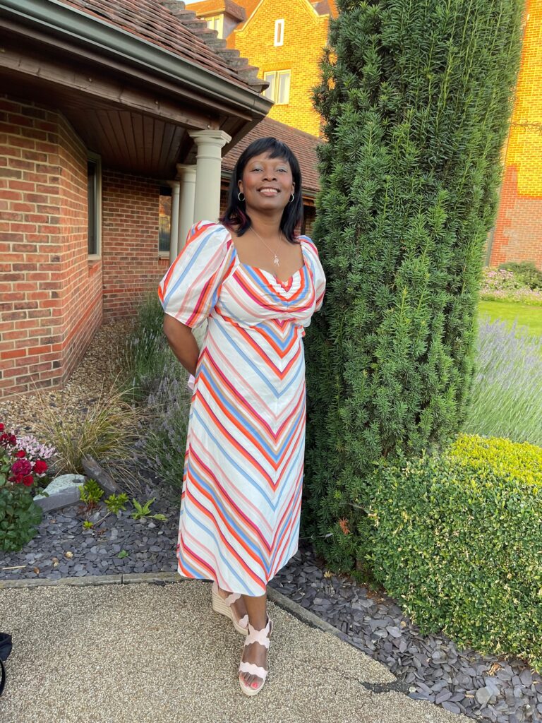Fleur smiles, wearing a striped dress in a garden.