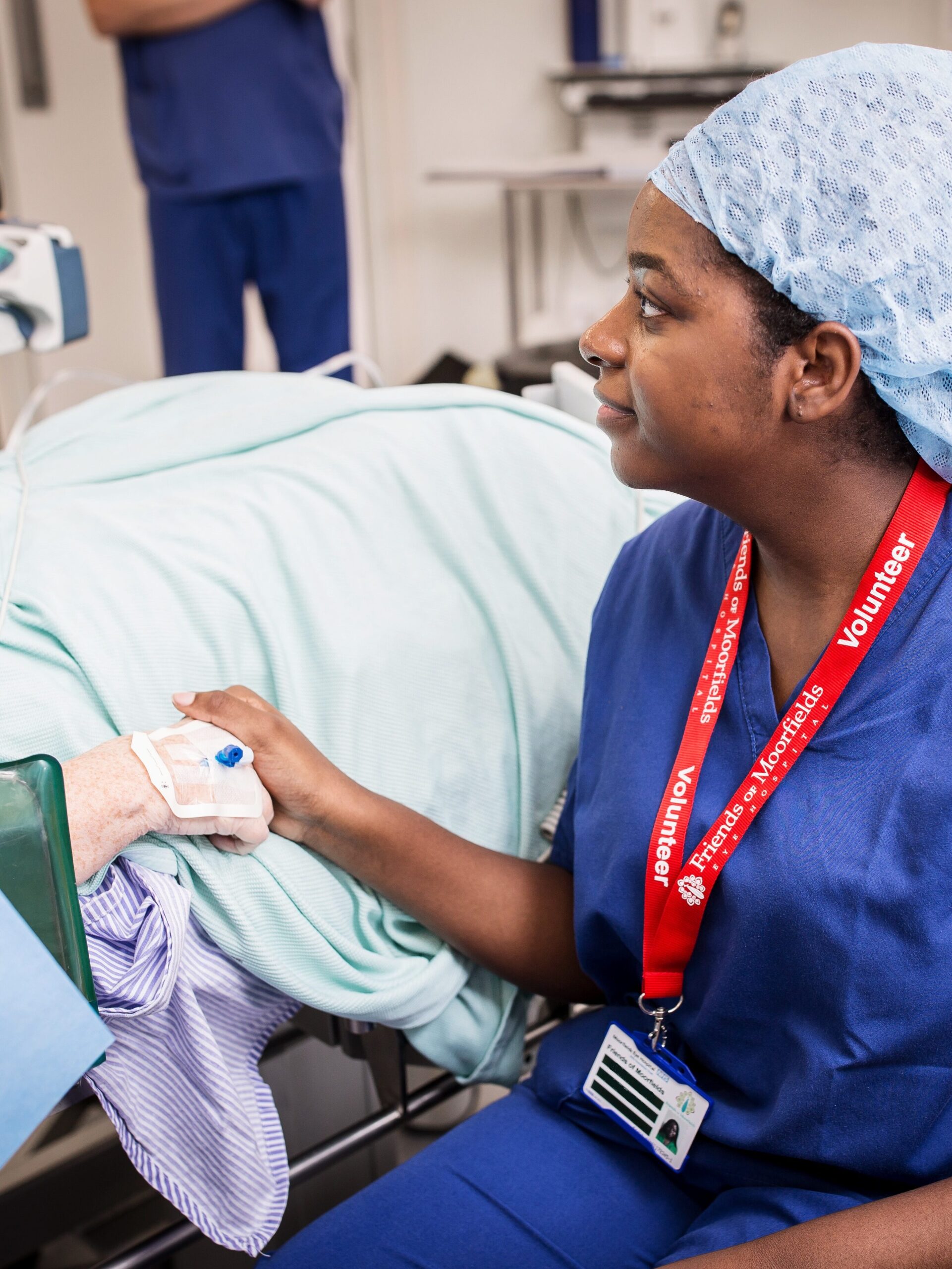 A volunteer smiles as she holds a patient's hand.