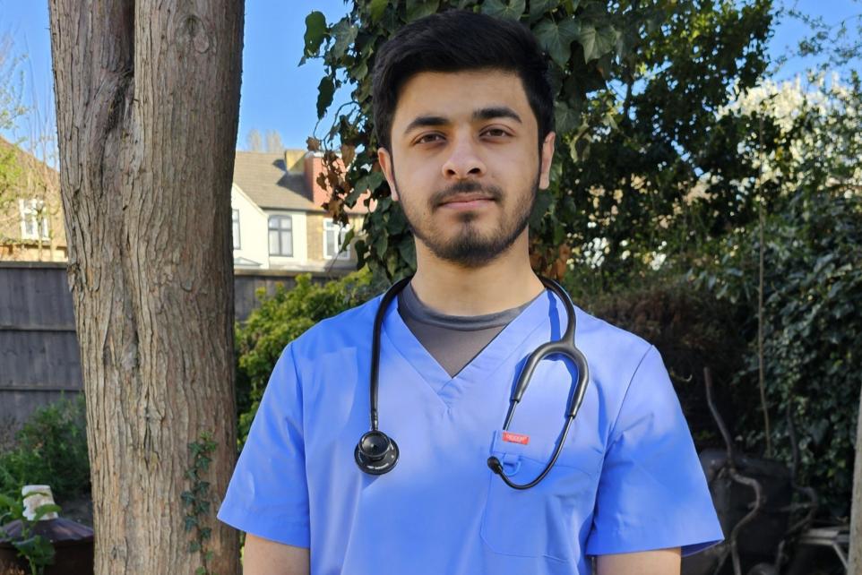 Raahat, wearing scrubs, stands smiling in a garden.
